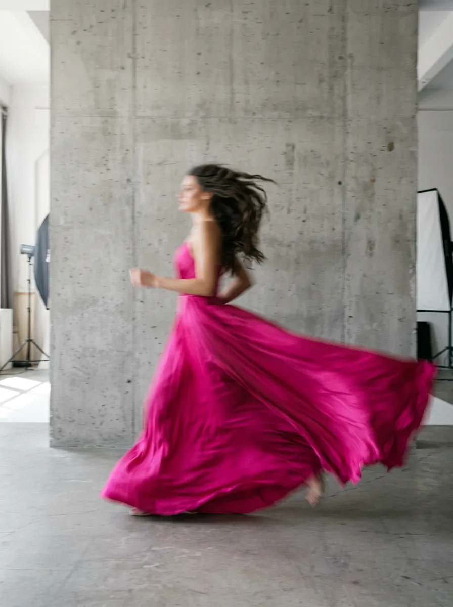 A woman in a flowing pink gown runs past a concrete pillar